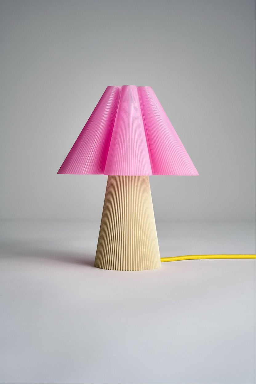 Layerd Bloom Flush table lamp with a pink pleated shade and a cream pleated base. Yellow cord visible.
