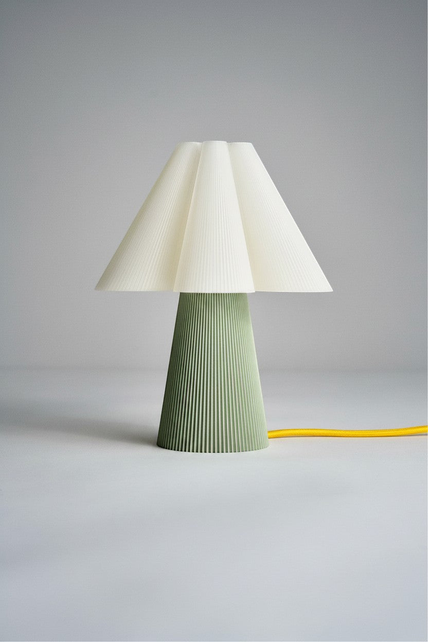 Layerd Bloom Sage table lamp with a pleated cream shade and a green pleated base. Yellow cord visible.